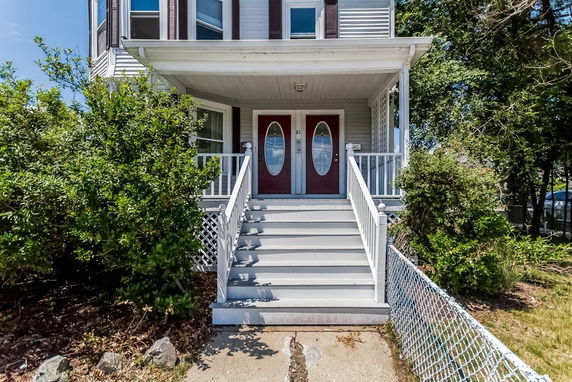 Front view of a house with a covered porch and red double doors, accessible by a short flight of stairs.