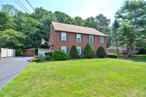 Front view of a two-story house with an American flag and greenery.