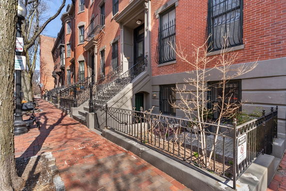 Front view of a row of brick townhouses with decorative iron railings and steps.