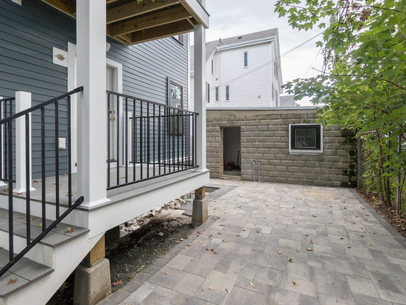 Side view of a two-story house with a small porch and a paved patio area.
