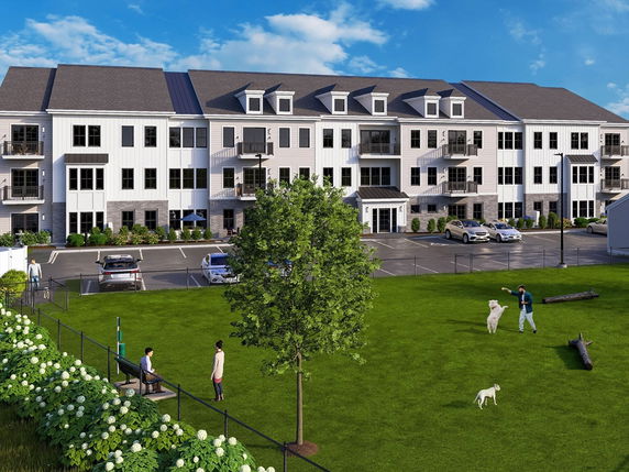 Front view of a multi-story residential building with parking area and green lawn.