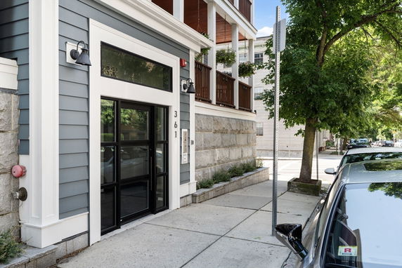 Front entrance view of a multi-story building with gray siding and glass doors.