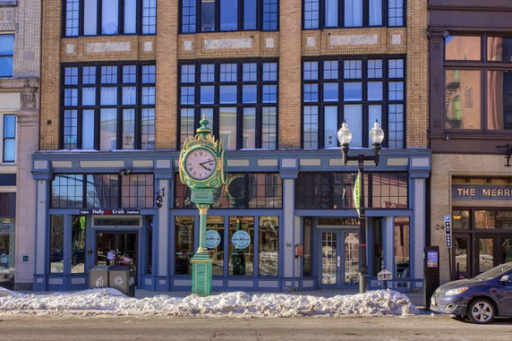 Front view of a multi-story brick building with large windows and a clock on a pole in front.