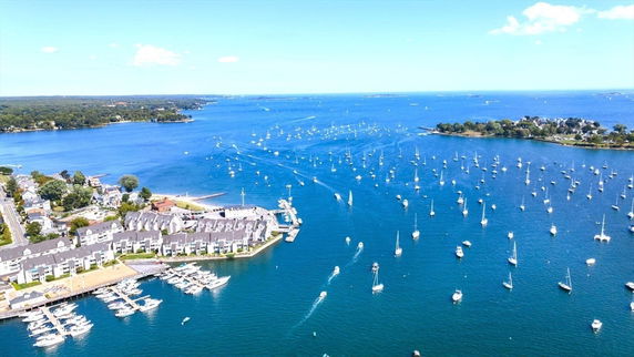 Wide aerial view of a coastal area with numerous boats on the water and residential buildings on the shore.