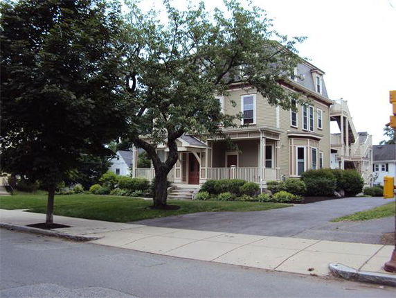 Front view of a large, multi-story house with bay windows and a porch.