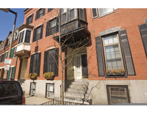 Front view of a multi-story brick townhouse with black shutters.
