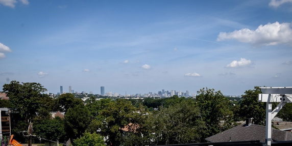 Panoramic view of a city skyline from a distance with trees and rooftops in the foreground.