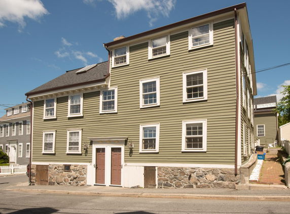 Front view of a three-story house with multiple windows and a stone foundation.