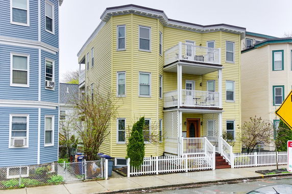Front view of a multi-story house with balconies and a picket fence.