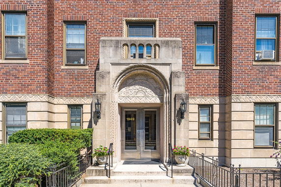 Front view of a brick building entrance with decorative stone arch and multiple windows.