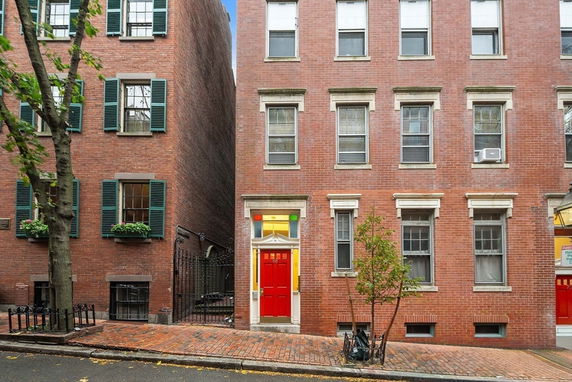 Front view of a brick townhouse with a red door and multiple windows.