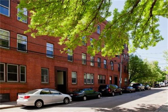 Front view of a multi-story brick building with several windows and parked cars on the street.