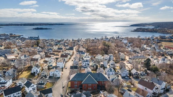 Aerial panoramic view of a coastal town with numerous houses and buildings, overlooking a body of water.