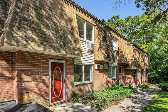 Front view of a two-story brick building with a red door and windows featuring air conditioning units.