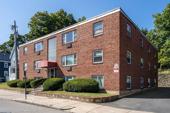 Front view of a brick apartment building with multiple windows and a red entrance canopy.