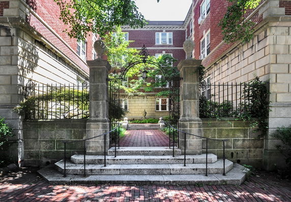 Front view of a brick building entrance with stairs and wrought iron gate.