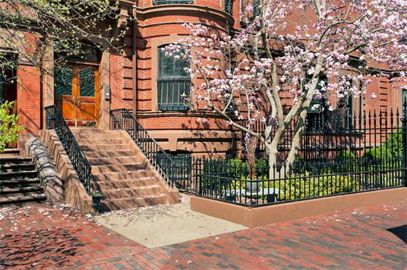 Front view of a three-story brick house with wrought iron fencing and a blooming tree.