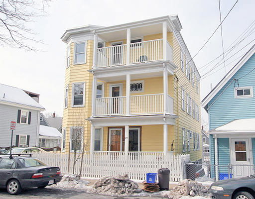 Front view of a three-story yellow house with multiple balconies and a white picket fence.