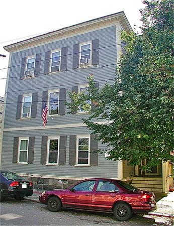 Front view of a three-story house with an American flag and parked cars.