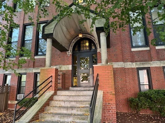Front view of a brick building with an arched entrance and stairs.