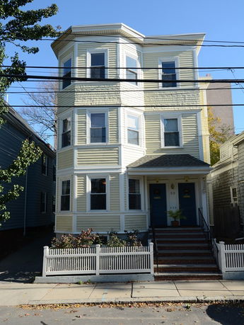 Front view of a three-story house with light yellow siding and a small porch.