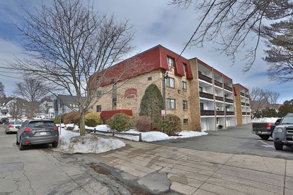 Front view of a multi-story apartment building with balconies and parking area.