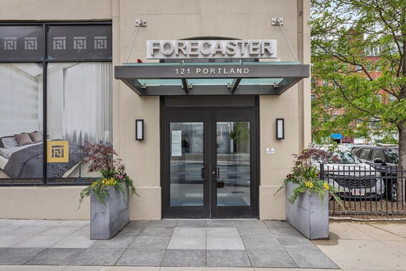 Entrance of a building with glass doors and a sign above reading 'Forecaster 121 Portland'.