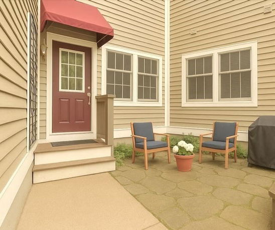 Front view of a house with an exterior door, windows, and a small patio with chairs.