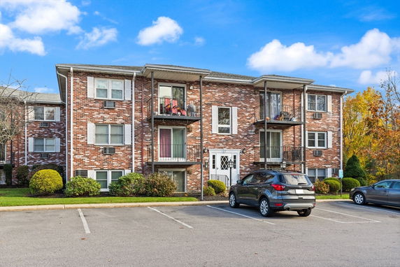 Front view of a three-story brick apartment building with balconies and a parking area.