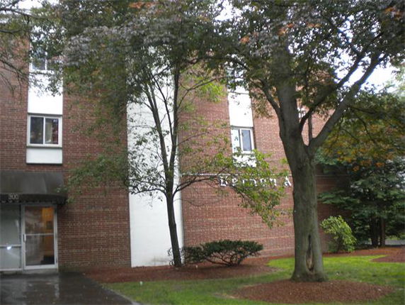 Front view of a brick apartment building with trees and a lawn area.