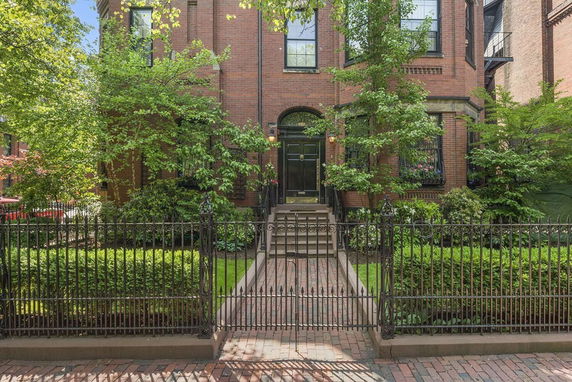 Front view of a classic brick house with a gated entrance and greenery.