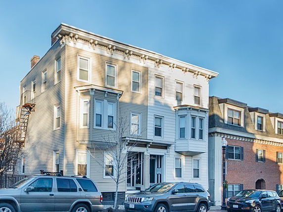 Front view of a three-story building with multiple windows and cars parked in front.