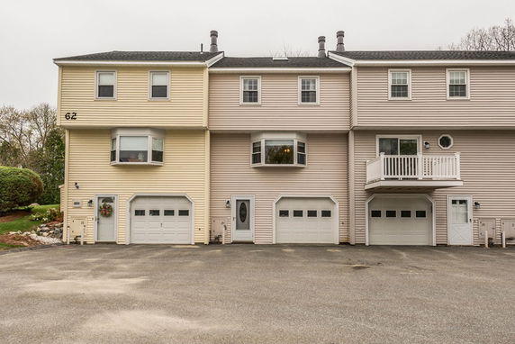 Front view of a townhouse complex with three connected units, each with a garage and multiple windows.