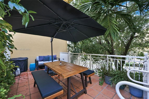 Outdoor seating area with large umbrella, wooden table, and benches, surrounded by greenery.