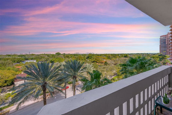 Panoramic view of surrounding areas from a balcony, showing trees and distant city skyline against a colorful sky.