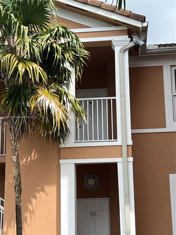 Front view of a two-story house with palm tree and balcony.
