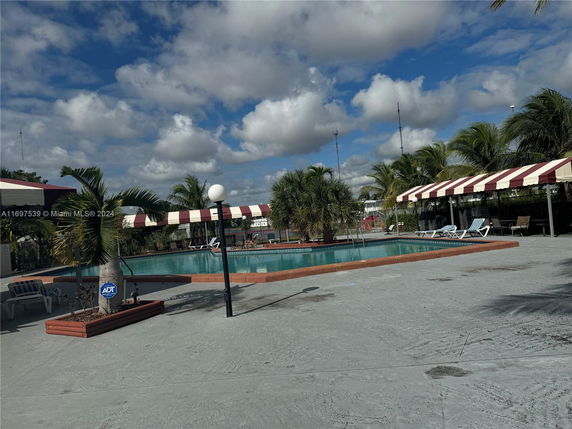 Outdoor swimming pool with poolside seating and striped canopies.
