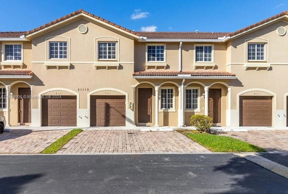 Front view of a two-story townhouse with attached garages and arched entryways.