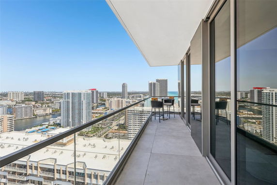 Balcony with glass railing offering a panoramic cityscape and ocean view.