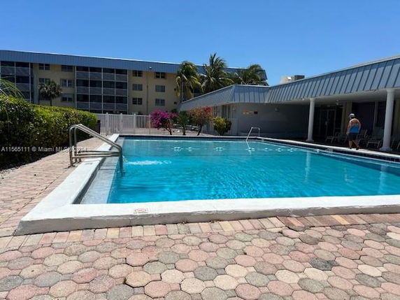 Outdoor swimming pool area adjacent to a building with shaded seating.