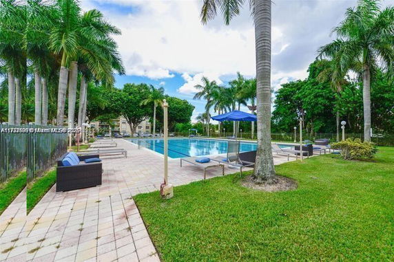 Outdoor swimming pool area with lounge chairs and parasols surrounded by palm trees.