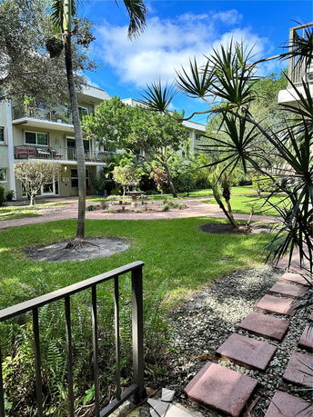 View of a multi-story apartment building with balconies surrounded by a grassy courtyard with trees and plants.