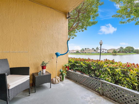 Patio area with wicker chair and decorative flamingo overlooking a waterfront with residential houses.