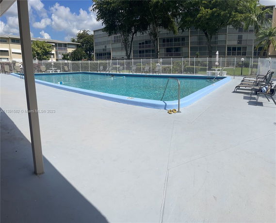Outdoor swimming pool area with surrounding fence and lounge chairs.