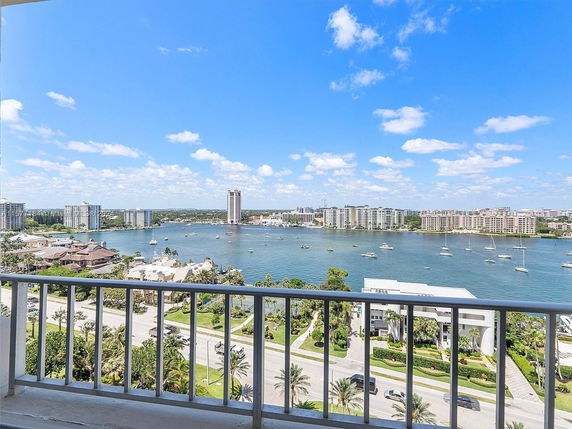 Panoramic view of a waterfront area with buildings and sailboats, seen from a balcony.