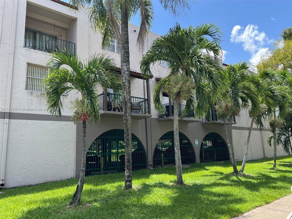 Front view of a multi-story building with balconies and arched entryways in a tropical setting.