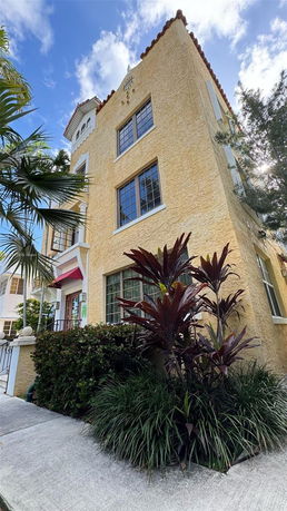 Front view of a multi-story building with yellow stucco walls and large windows.