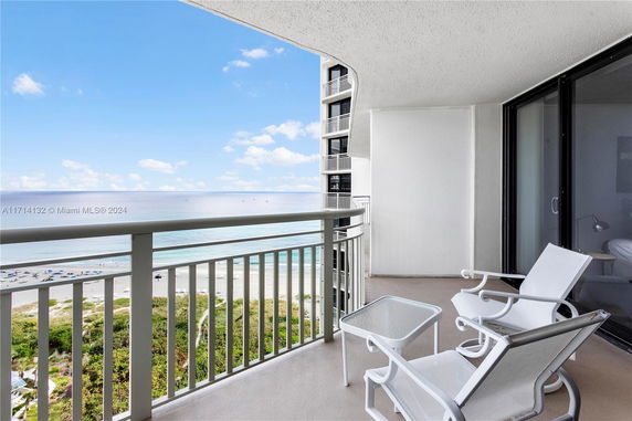 Balcony view showing beach and ocean with chairs and a table.