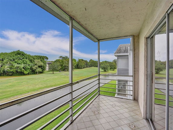 View from a balcony overlooking a grassy area with trees and a small body of water.