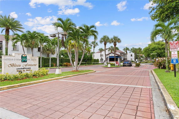 Front view of a condominium complex entrance with palm trees and signage.